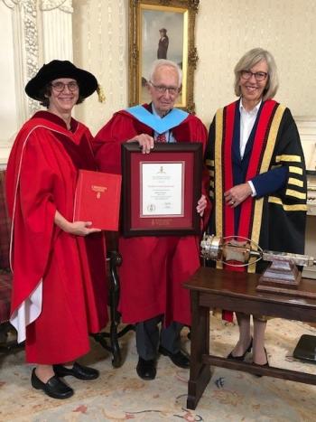 Stephen Jarislowsky is pictured receiving his honorary doctorate degree from the University of Guelph for his long-standing commitment to business ethics and accountability in corporate governance and to supporting the University of Guelph. Deborah Stienstra stands to his his left, and Dr. Charlotte Yates to his right. All three are wearing academic gowns, and are smiling widely.