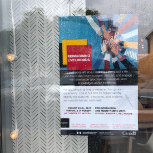 A poster for the Reimagining Livelihoods Forum is visible through a window, with string lights hanging on the inside and rain droplets splattered on the outside.