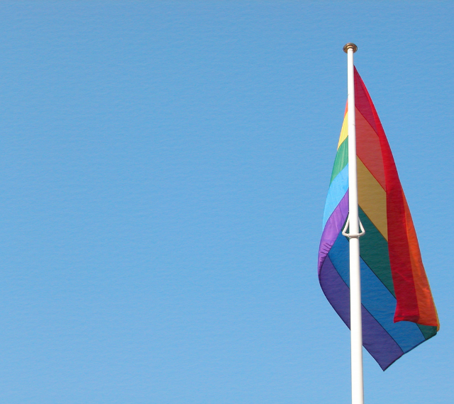 A blue sky with a rainbow Pride flag blowing in the breeze.