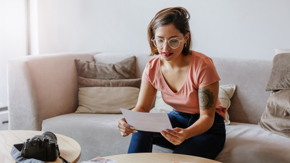 Young woman sitting on couch, looking at paper