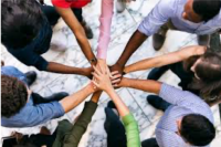 A group of 9 individuals putting their hands on top of each others in a circle.