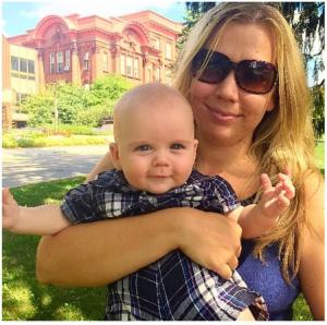 Blonde woman holder her baby in front of a house. 