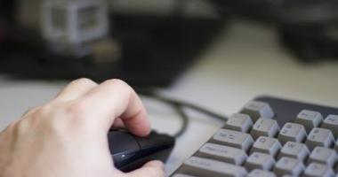 A white hand on a computer mouse beside a keyboard